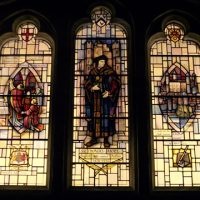 Stained glass design by A. E. Buss, M.G.P., Guildhall crypt, London. Photograph by Nick Wignall. More, Bible in hand, is standing before the gates of St. James' Palace. His family Arms are shown at the head of the light. Guildhall Crypt stained glass- Sir Thomas More, 1971